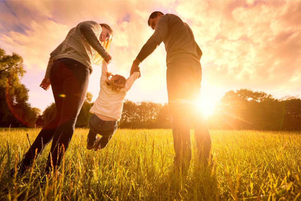 Parents hold the baby’s hands.  Happy family in the park evening light. The lights of a sun. Mom, dad and baby happy walk at sunset. The concept of a happy family.